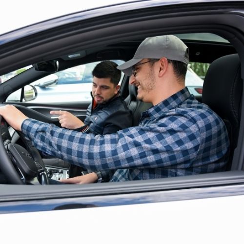 Deux personnes échangent à bord d’une voiture lors d’une démonstration ou d’un essai de véhicule.