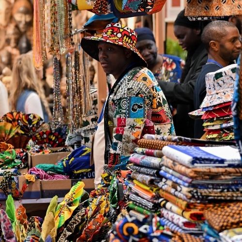 Un vendeur présente des tissus et accessoires colorés sur un stand de marché culturel.