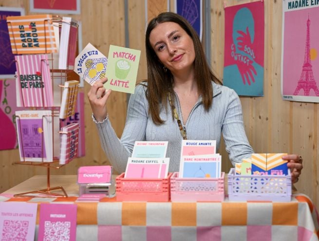 Une exposante présente ses cartes colorées et originales lors de la Foire de Paris, entourée de son stand aux teintes pastel.